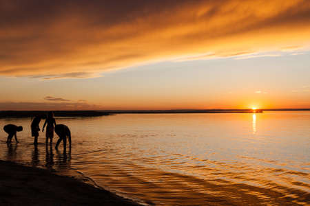 Silhouette of kids playing on the beach water's edge during sunset. Silhouette outlines modified in Photoshop to render persons unidentifiable.の写真素材