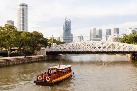 A boat ply the Singapore River on Boat Quay toward Anderson Bridge, with the city's skyline in the background.の写真素材