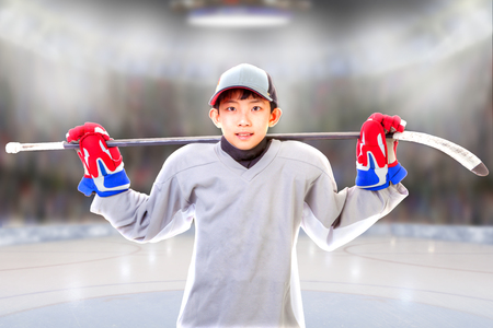 Junior hockey player posing on ice in sports arena with hockey stick across shoulder. Shallow depth of field on background and copy space.の写真素材