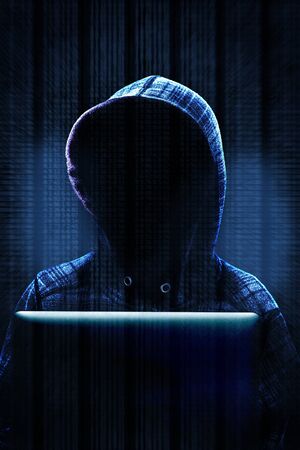 Unknown computer hacker with hood working on computer laptop in committing cyber crime on the Internet. Background data and dramatic lighting with copy space.の写真素材