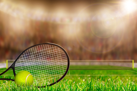 Low angle view of tennis racket and ball on grass court with deliberate shallow depth of field on brightly lit stadium background and copy space.の写真素材