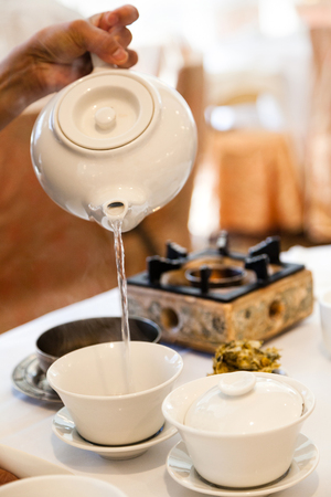 Pouring hot water into Chinese tea cup for steeping and brewing tea during traditional dim sum meal.の写真素材