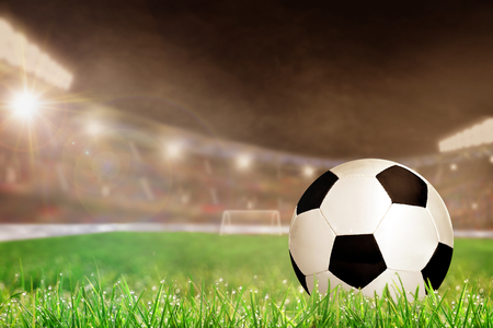 Soccer ball on field grass in brightly lit outdoor stadium with focus on foreground and shallow depth of field on background. Deliberate lens flare and copy space.の写真素材