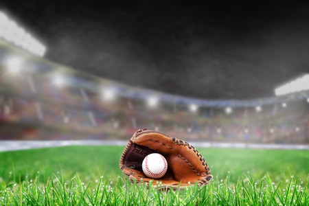 Baseball glove and ball on grass in brightly lit outdoor stadium with focus on foreground and shallow depth of field on background. Deliberate lens flare and copy space.の写真素材