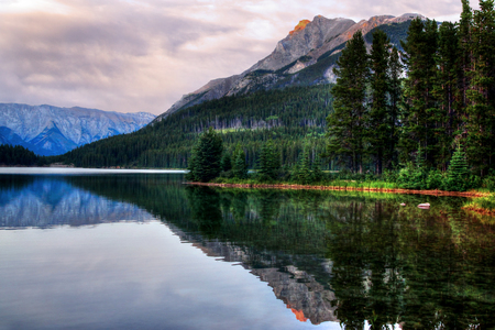 Sunset at Two Jack Lake in Banff National Park with sunlit mountain range in the background reflecting off the calm waters.の写真素材
