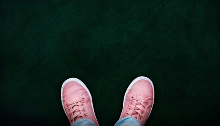 A teenage girl in jeans and pink canvas shoes standing on empty chalkboard with copy space. Concept of standing at the crossroads to contemplate a decision.の写真素材