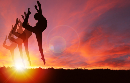Silhouette of girls dancing and jumping with vibrant golden sunrise or sunset background and copy space. Concept of healthy living, exercising, celebration or jubilant mood.の写真素材