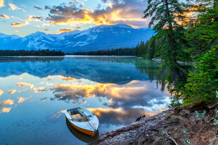 Morning sun breaks out over the Rocky Mountains at Edith Lake in Jasper National Park, with a boat in the foreground.の写真素材