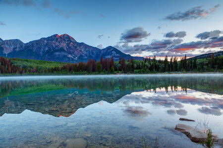 Early morning sunrise at Patricia Lake with the golden sunlit Pyramid Mountain in the background and misty fog on the water's surface. Wide angle shot.の写真素材
