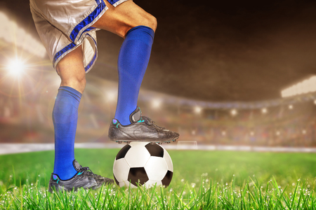 Soccer player in action with football in brightly lit outdoor stadium. Focus on foreground and soccer ball with shallow depth of field on background and copy space.の写真素材