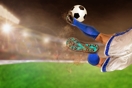 Soccer player with spectacular scissor kick of football in brightly lit outdoor stadium. Focus on foreground and soccer ball with shallow depth of field on background and copy space.の写真素材