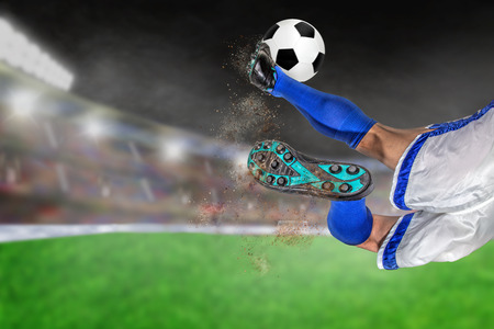 Soccer player with spectacular scissor kick of football in brightly lit outdoor stadium. Focus on foreground and soccer ball with shallow depth of field on background and copy space.の写真素材