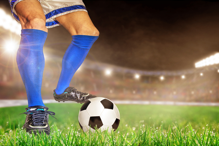 Soccer player in action with football in brightly lit outdoor stadium. Focus on foreground and soccer ball with shallow depth of field on background and copy space.の写真素材
