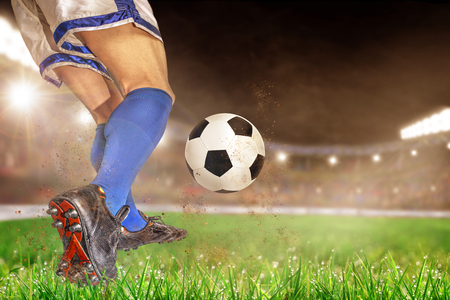 Soccer player in action with football in brightly lit outdoor stadium. Focus on foreground and soccer ball with shallow depth of field on background and copy space.の写真素材