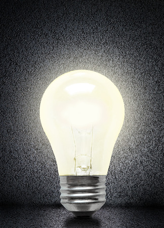 Glowing electrical incandescent light bulb isolated on asphalt background with copy space.の写真素材