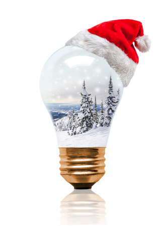 Snow globe light bulb wearing Santa hat with Christmas Winter scene with copy space. Glowing Xmas season and bright New Year.の写真素材
