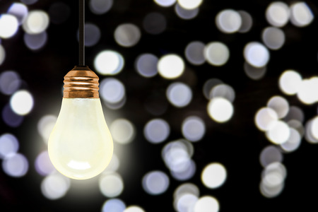 Illuminating light bulb hanging with colorful blurred Christmas lights bokeh effect and copy space.の写真素材