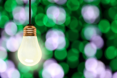 Illuminating light bulb hanging with colorful blurred Christmas lights bokeh effect and copy space.の写真素材