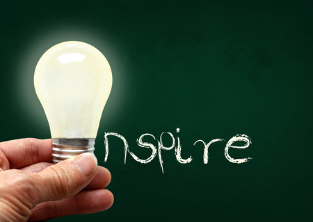 Man holding illuminated bulb with bare hands against chalkboard with the word Inspire. Concept of bright idea, innovation, imagination, inspiration, vision. Copy space.の写真素材