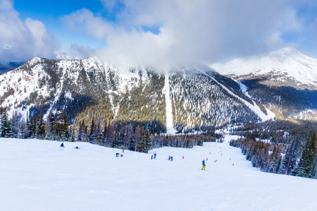 Unidentifiable skiers and snowboarders at a distance going down a mountain slope in Lake Louise in the Canadian Rockies of Alberta, Canada.の写真素材