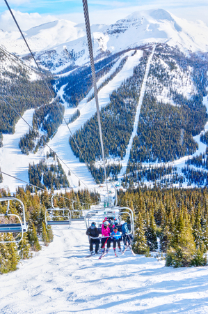 Unidentifiable skiers on chairlift going up a ski slope in the snowy mountain range of the Canadian Rockies.の写真素材