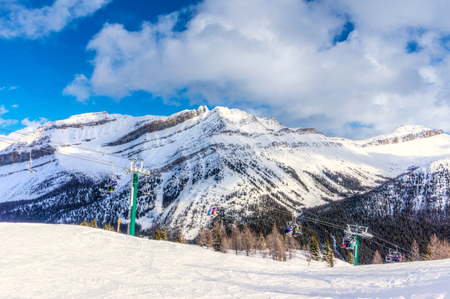 Unidentifiable skiers and snowboarders on chairlift going up a ski slope in the snowy mountain range of the Canadian Rockies.の写真素材