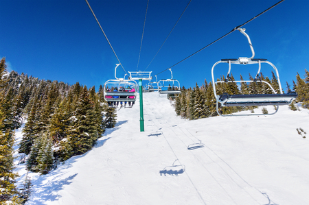 Unidentifiable skiers on chairlift going up a ski slope in the snowy mountain range of the Canadian Rockies.の写真素材