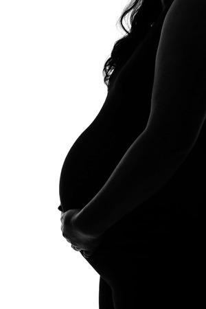Silhouette of young mother with hands holding her pregnant tummy. Side profile view in black and white with copy space.の写真素材