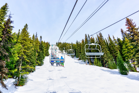Unidentifiable skiers on chairlift going up a ski slope in the snowy mountain range of the Canadian Rockies.の写真素材