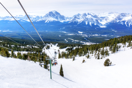Unidentifiable skiers on chairlift going up a ski slope in the snowy mountain range of the Canadian Rockies.の写真素材