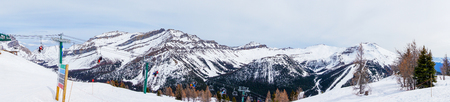 Wide angle panorama of skiers and snowboarders on chairlift going up a ski slope in the snowy mountain range of the Canadian Rockies at Lake Louise.の写真素材