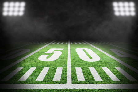 Close up of American football field with stadium spotlight on specific 50 yard markings and background smoke with copy space.の写真素材