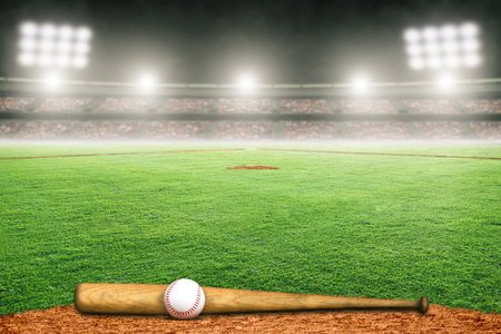 Baseball bat and ball on field at brightly lit outdoor stadium. Focus on foreground and shallow...