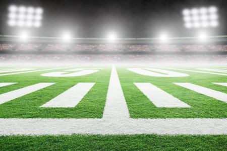 Close up of American football stadium field with yard line markings and spotlight with blurred...