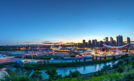 CALGARY, CANADA - JULY 14, 2019: Panorama of golden sunset over the Calgary Stampede fairgrounds surrounded by the Bow River with the city's urban skyline in the background. The city's iconic Calgary Tower and Saddledome can also be seen.のeditorial素材