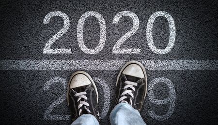 A teenager in jeans and canvas shoes standing on asphalt road ready to step from 2019 into New Year 2020. Concept of new beginning or directions in a new year ahead.の写真素材