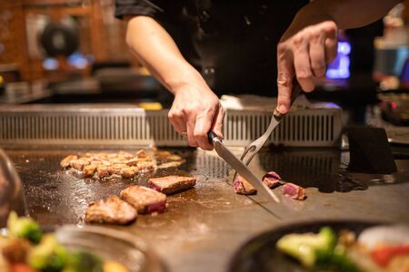 Teppanyaki chef cooking Japanese Wagyu beef and filet mignon steak on hot metal plateの写真素材