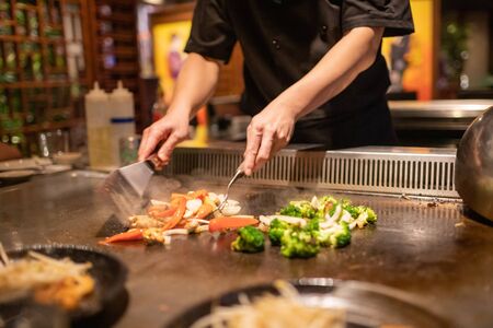 Teppanyaki chef preparing Japanese cuisine on hot metal plate by cutting up vegetablesの写真素材