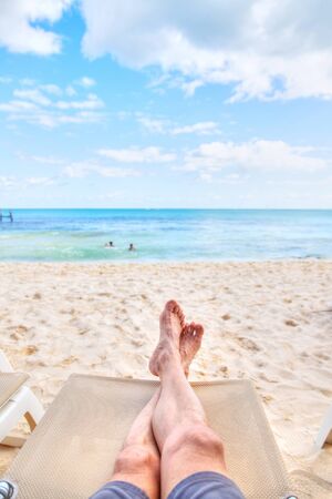 Personal perspective of man relaxing on a lounge chair at sandy beach with crossed legs view towards sea view and copy space. Shot taken in the Caribbean coast of Mexico at Cancun.の写真素材
