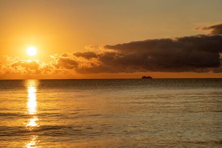 Golden sunrise over the Caribbean Sea as seen from the coast of Cancun, Mexico, with a silhouette of a passing ship in the distance.の写真素材