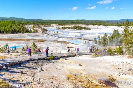Unrecognizable visitors walking on the Porcelain Basin boardwalk trail surrounded by geothermal pools inside Norris Geyser Basin of Yellowstone National Park, Wyoming, USA.の写真素材