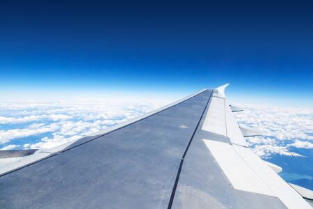 Airplane window view showing wing of plane flying above the clouds.の写真素材