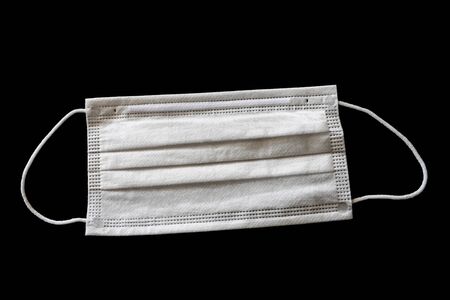 White surgical face mask isolated on black background. Concept of controversial mask use duirng Covid-19 coronavirus pandemic.の写真素材