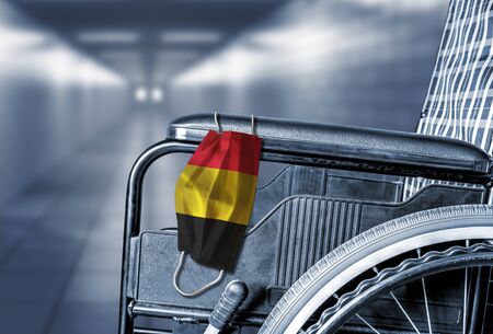 Flag of Belgium on face mask hanging on empty wheelchair in hallway of Belgian hospital or retirement nursing care home with copy space. Concept of healthcare at long term care homes during pandemic. 90 percent of Belgium care homes have COVID-19 cases.の写真素材