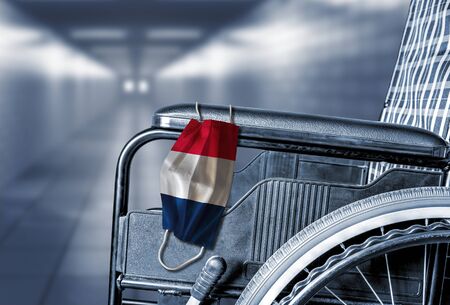 Flag of France on face mask hanging on empty wheelchair in hallway of French hospital or retirement nursing care home with copy space. Concept of healthcare at long term care homes during pandemic.の写真素材