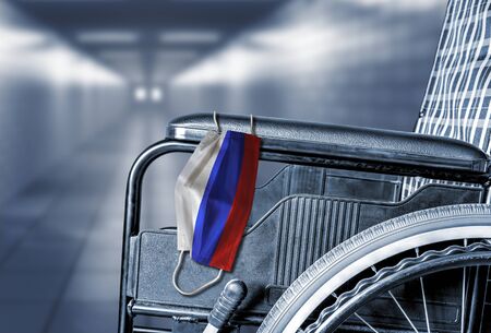 Flag of Russia on face mask hanging on empty wheelchair in hallway of Russian hospital or retirement nursing care home with copy space. Concept of healthcare at long term care homes during pandemic.の写真素材