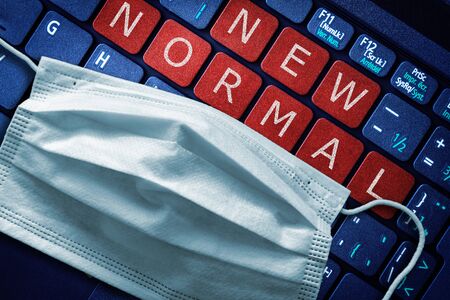COVID-19 coronavirus lockdown restrictions ease concept showing New Normal on laptop red alert button with surgical face mask on keyboardの写真素材