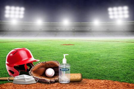 Baseball equipment on field of an empty stadium with hand sanitizer and medical face mask. Concept of baseball played without fans as part of social distancing to prevent spread of COVID-19 coronavirus in the New Normal.の写真素材