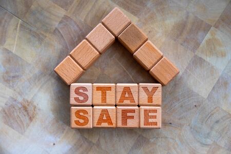 Stay home to stay safe due to Covid-19 coronavirus outbreak pandemic. Concept of self isolation or quarantine message engraved on wooden blocks on wood background with copy space.の写真素材