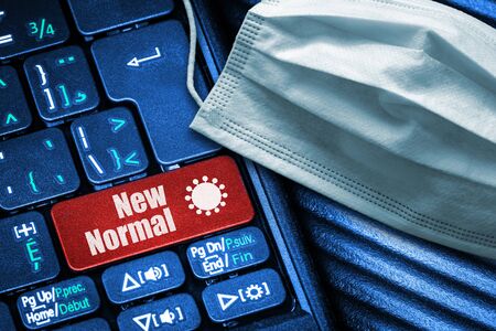 Concept of New Normal following Covid-19 reopening of economy and returning to work as illustrated by computer keyboard with red button text and face mask.の写真素材